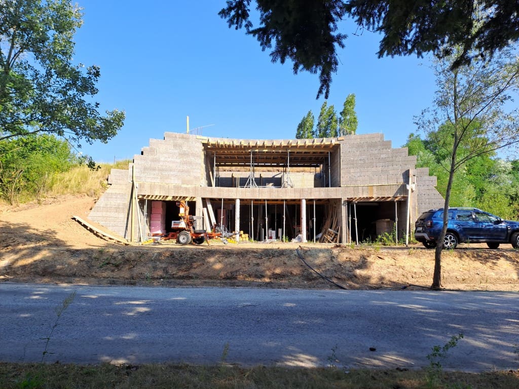 Partly built earth-sheltered house with stepped concrete blocks set into a grassy hillside, construction equipment in front