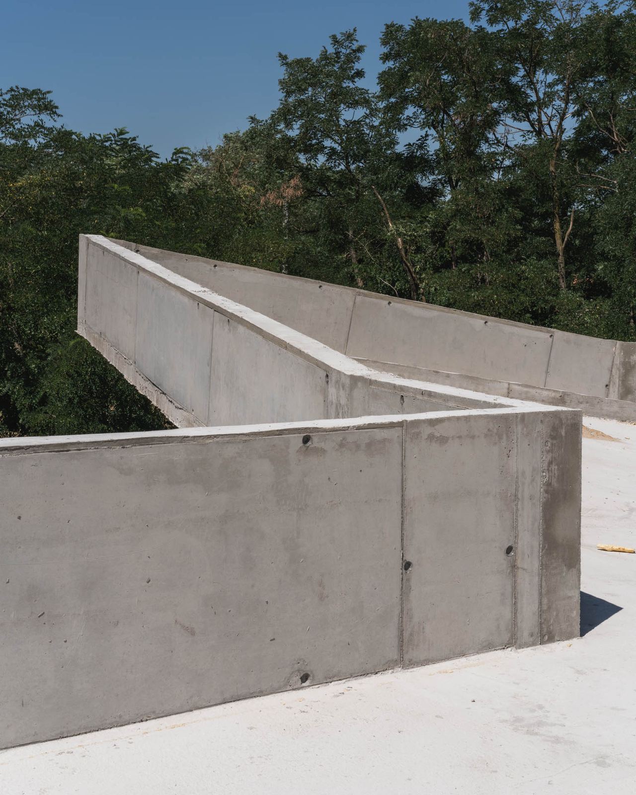 Raw board-formed concrete retaining walls zigzag on a wooded earth-sheltered house construction site