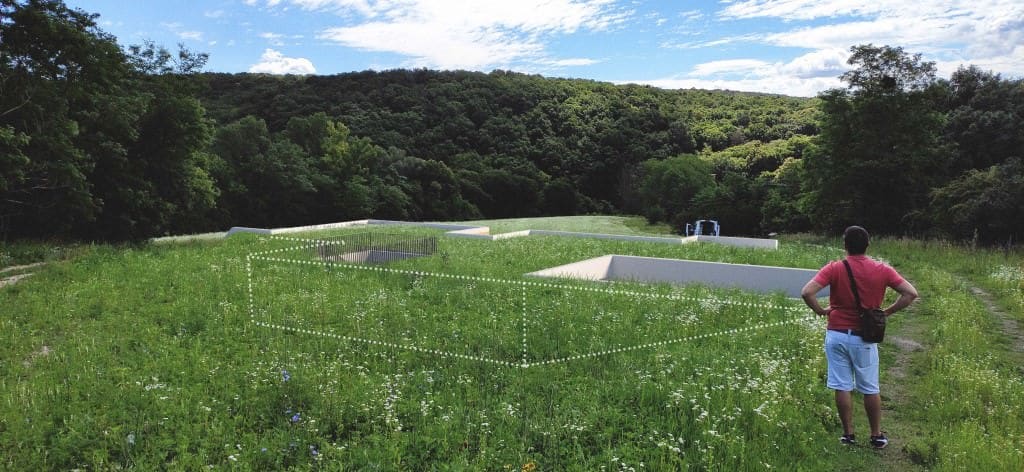 Aerial view of an earth-sheltered house under construction in a meadow, with a dotted overlay showing the planned building footprint