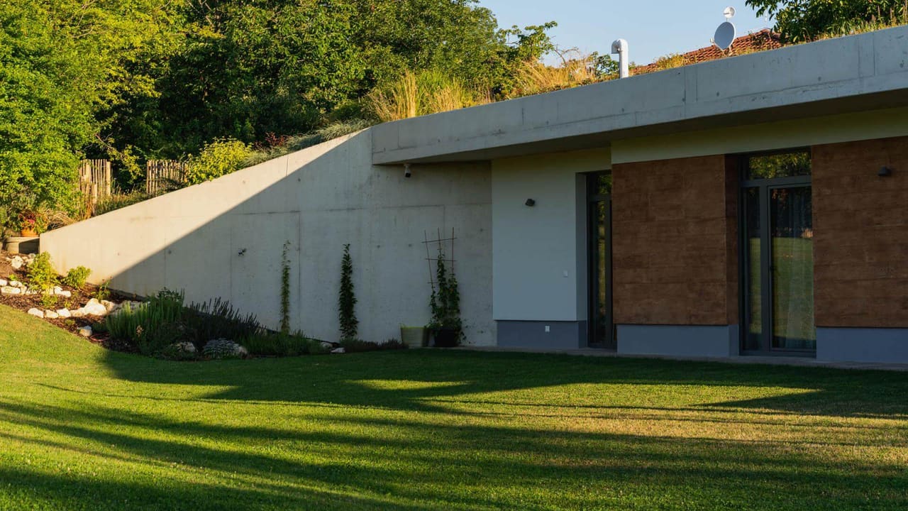 Earth-sheltered home at sunset: green roof meets board-formed concrete wall beside wood-paneled living wing