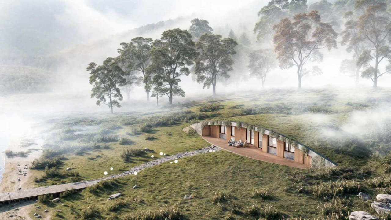 Earth-sheltered hobbit-style home with grass roof and wood deck by a misty lakeside forest